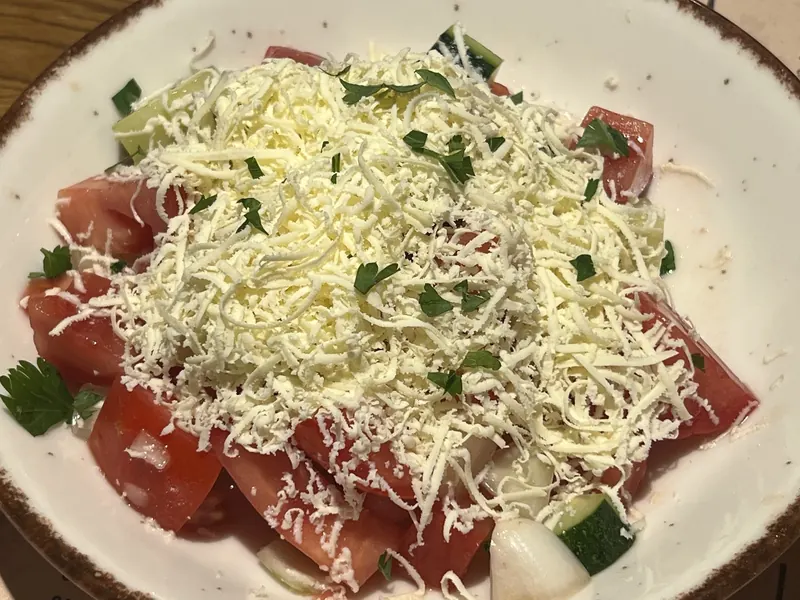 Shopska salad: tomato and cucumber under a heap of grated white cheese and parsley