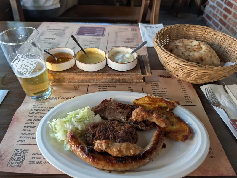 A mixed grill plate with sausage, qofte and chicken, three sauces, a Jack's beer and bread