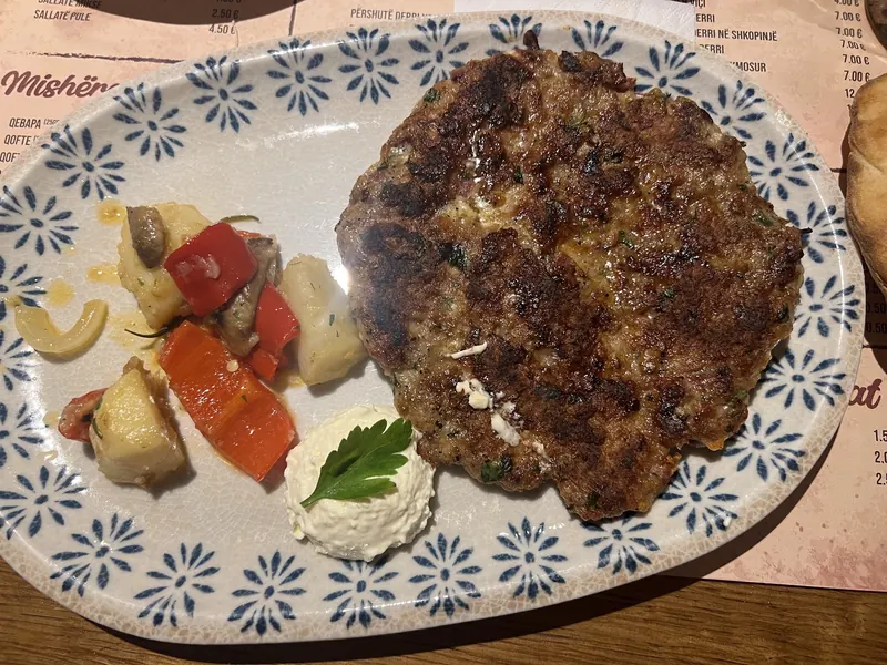 A large grilled qofte with roasted vegetables and a spoon of kajmak