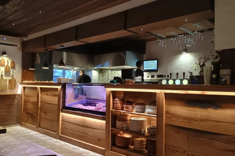 The open counter at Jaki Grill: a lit glass case of fresh meat, stacked plates and the kitchen behind