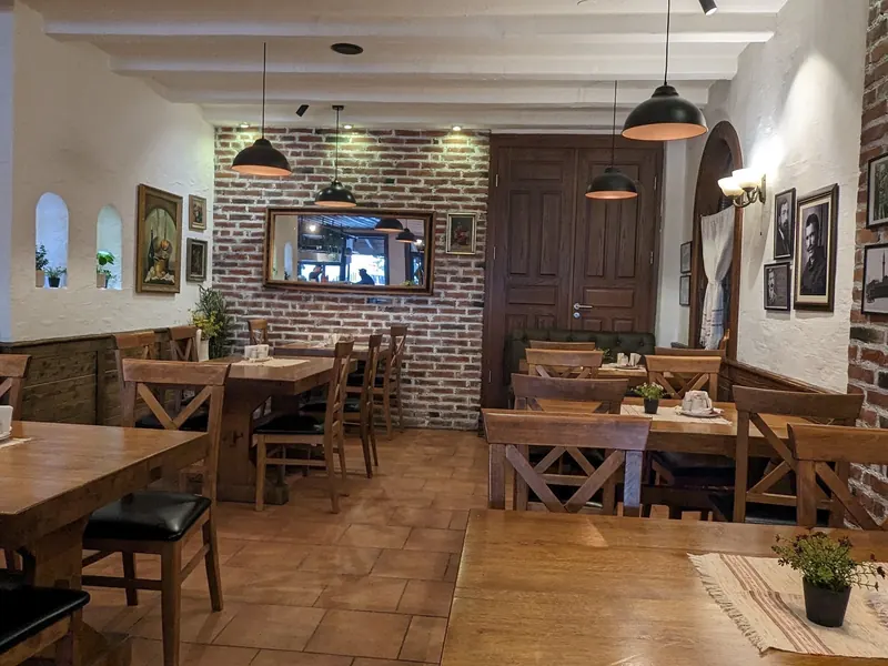 The dining room with wooden tables, pendant lamps, a brick wall and framed portraits