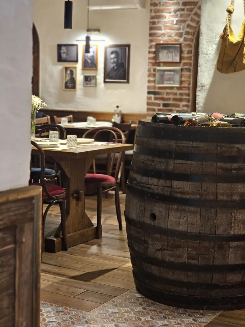 An old wine barrel between tables, with framed black-and-white portraits on the brick and plaster walls